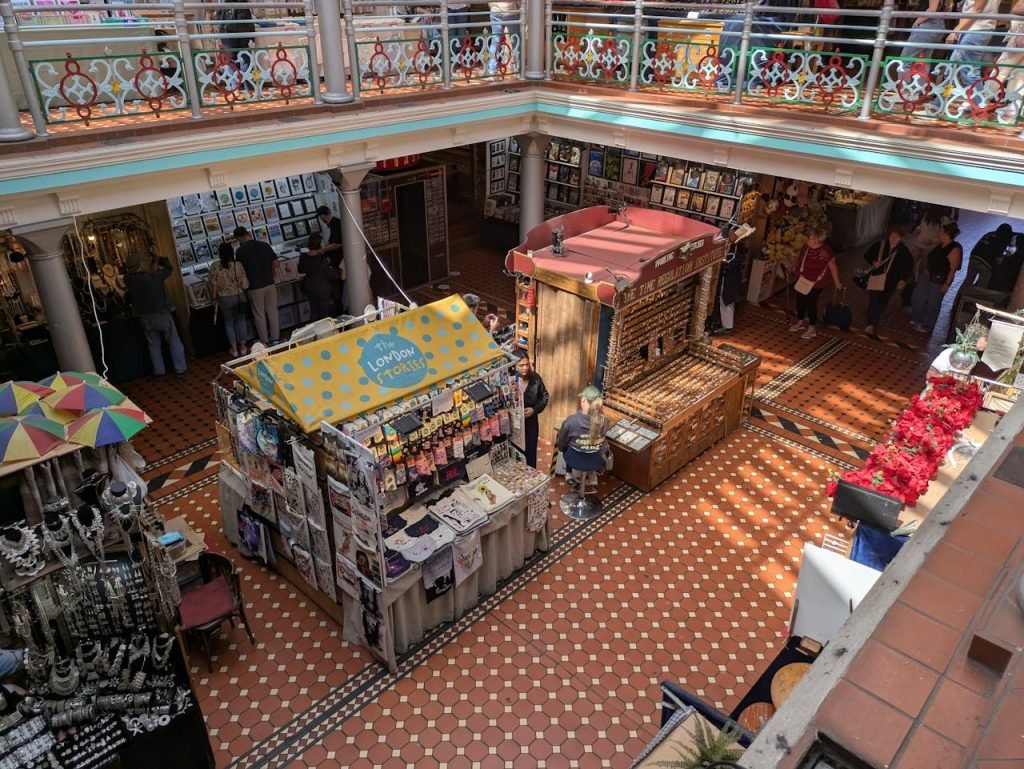 Vibrant view of a bustling indoor market in London arcade with various stalls and shoppers.